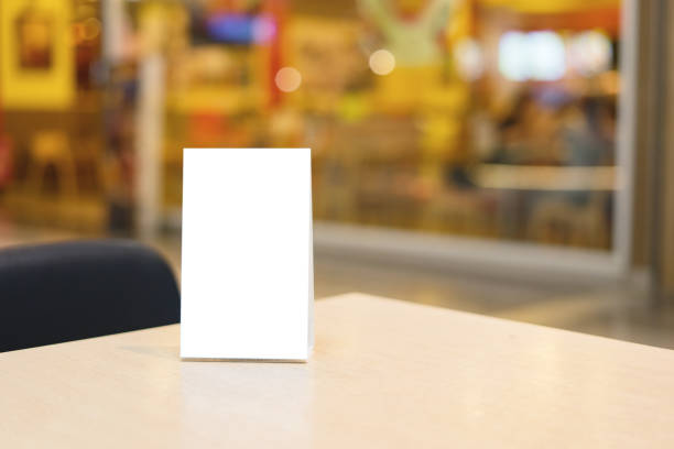 istock Mock up Label the blank menu frame in Bar restaurant ,Stand for booklets with white sheets paper acrylic tent card on wooden table cafeteria blurred background can inserting the text of the customer. 1200501977