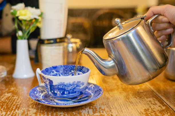 Hands pouring tea from a teapot into a cup stock photo