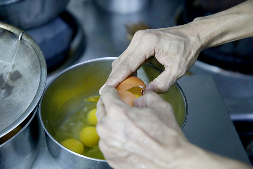 A Myanmar ethnicity male adult chef is cracking an chicken egg into a bowl in Kuala Lumpur commercial kitchen, Malaysia.