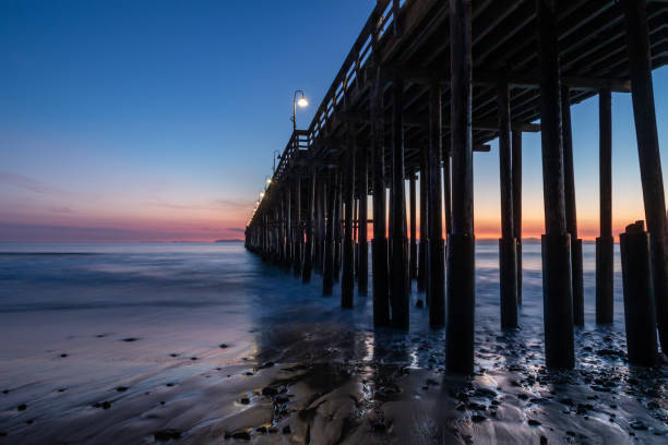 istock Ventura Pier at Sunset. Beach with rocks in foreground, smooth ocean; colored sky in background. 1200512276