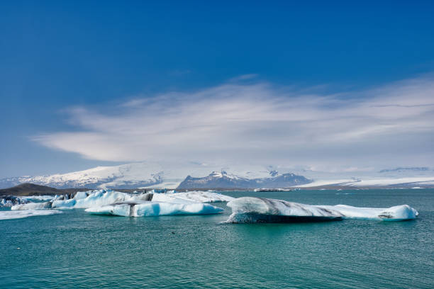istock Broken off calved ice floes or ice bergs with black streaks from volcanic ash make there way out of a deep lagoon as the head to the open North Atlantic Ocean 1200516140