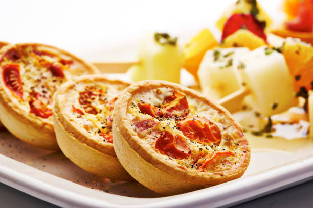Shot of miniature quiche lorraine with tomato, bacon and vegetable skewers served in a plate