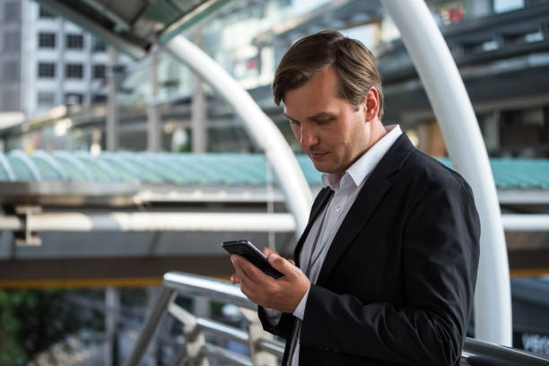 istock American professional businessman using smart phone. Middle-aged manager holding mobile smartphone using app texting outside office buildings. 1200525302