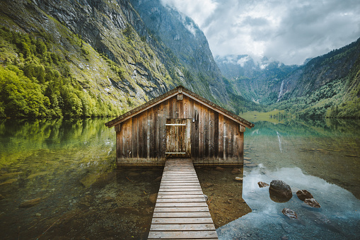Panoramic view traditional old wooden boat house at scenic Lake Obersee on a beautiful day with blue sky and clouds in summer, Bavaria, Germany