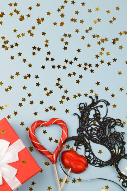 red gift, lollipops, decoration and black mask on blue background with small stars.