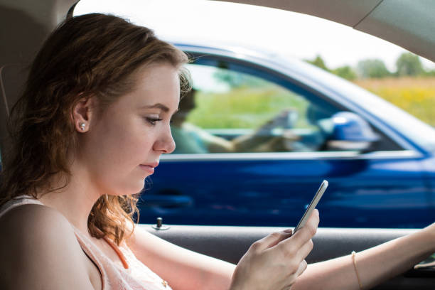 una joven conduce un coche y escribe un sms - careless fotografías e imágenes de stock
