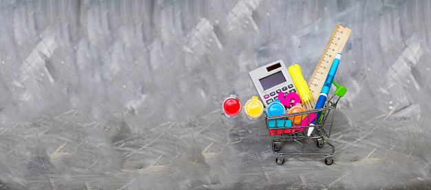 Shopping cart for school supplies on a gray background. Copy space.
