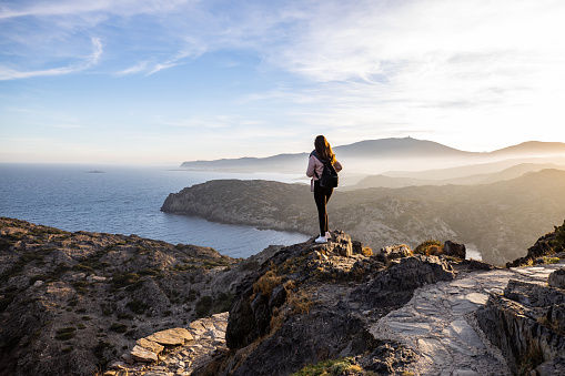 Hermosa mujer de pie en un acantilado durante la puesta de sol con el mar Mediterráneo al fondo en el Cap de Creus, en España con espacio de copia photo