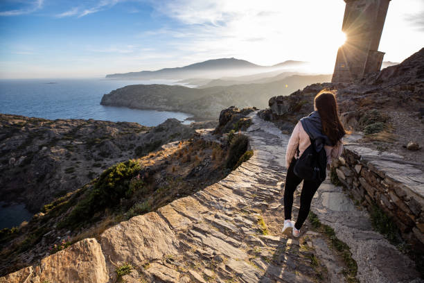 Beautiful woman standing on a cliff during sunset with the mediterranean sea in the background at Cap de Creus, in Spain with copy space Beautiful woman standing on a cliff during sunset with the mediterranean sea in the background at Cap de Creus, in Spain with copy space cap de creus stock pictures, royalty-free photos & images