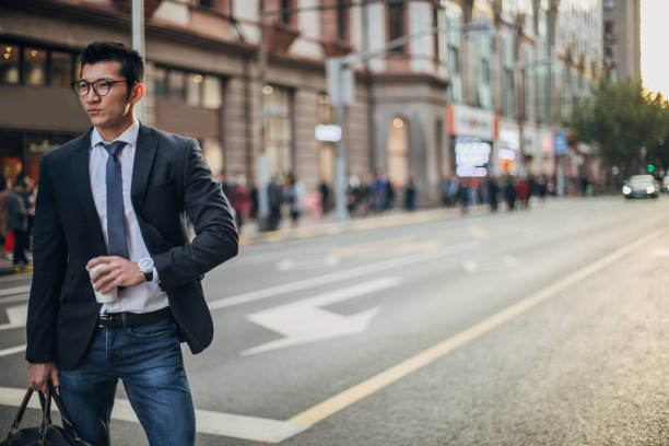 Young, elegant man in suit is drinking takeaway coffee on the street.