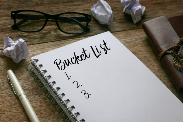Pen,trash paper,sunglasses, and notebook written with Bucket List on wooden background. stock photo