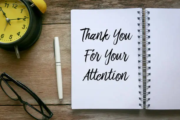 Top view of clock,glasses,pen and notebook written with Thank You For Your Attention on wooden background.