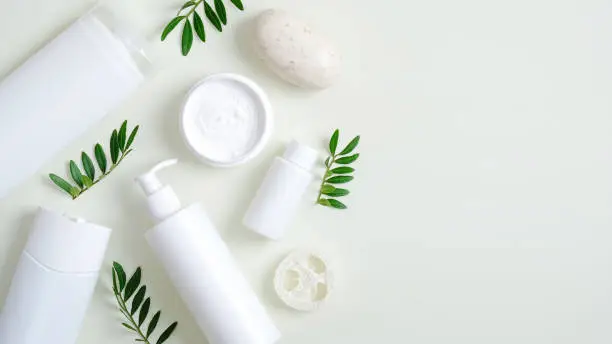 Photo of Organic herbal cosmetic products on green background. Top view beauty spa cosmetic bottle packaging, hand cream, lotion, bath sponge, natural soap and green leaves. Minimalist beauty product mockups