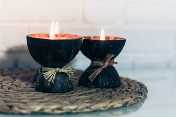 istock Burning spa aroma candles in coconut shell on wicker stand on a glass white table, cozy home interior background 1200560709