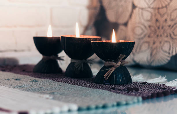 istock Burning spa aroma candle in coconut shell on a knitted multicolored rug and gray curtains opposite the white wall, cozy home interior 1200560711