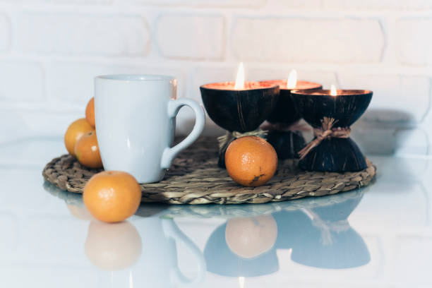 istock Burning spa aroma candles in coconut shell, tangerines on wicker stand on a glass white table, cozy home interior background top view 1200560787