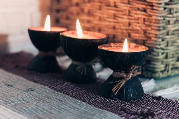 istock Burning spa aroma candle in coconut shell on a knitted multicolored rug and wicker box with a towel opposite the white wall, cozy home interior 1200560810