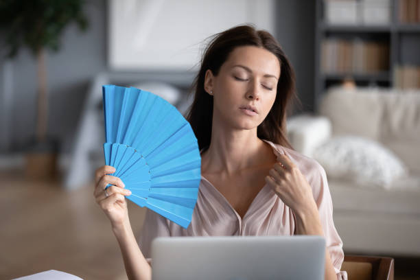 Stressed young woman use waver suffering from hot weather Stressed young woman sit at desk in living room feel warm use hand waver, unwell sick millennial girl wave fresh air at home suffer from hot weather, lack of air condition, heatstroke concept overheated photos stock pictures, royalty-free photos & images