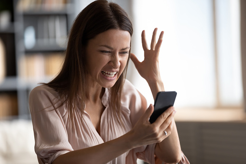 Mad young woman look at smartphone screen have operational gadget problems, angry millennial female feel stressed frustrated with slow Internet connection, bad service on modern cellphone device