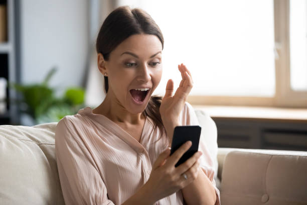 Amazed girl shocked by online win on cell Amazed young woman sit on couch at home feel shocked reading unexpected good news on cellphone gadget, stunned millennial girl surprised by online lottery win on smartphone, luck concept luck photos stock pictures, royalty-free photos & images