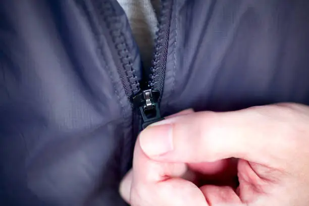Photo of Person hand zipping up zipper on his jacket.