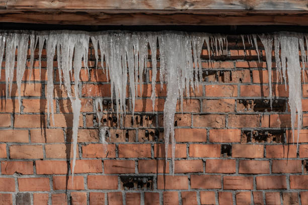 istock A beautiful horizontal texture of part of a old crashed brick wall in orange hue with a group of sharp white icicles is hanging down from the gray roof of a building in winter 1200571885
