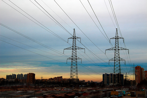 Metal pylons of power lines towering over the city against the sunset sky