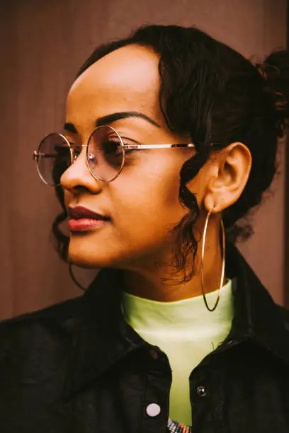 Side view close-up portrait of a beautiful young and confident African American woman with trendy accessories as round earrings and eyeglasses looking away while thinking of future plans