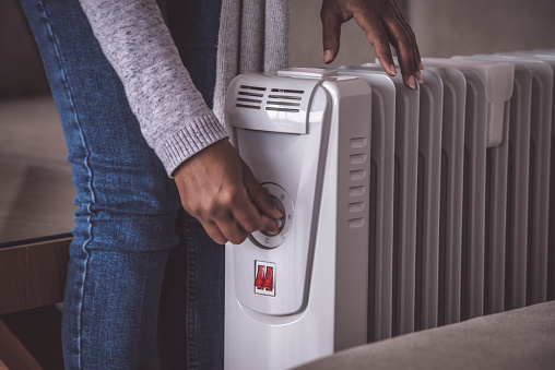 Close up image of female's hand rotating rotary switch to increase / decrease the temperature of an electric heating radiator (action in motion). The woman standing at the domestic room, touching on/off the rotate button.