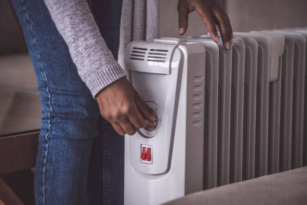 Increasing / decreasing power of an electric heater radiator at the cold winter season. Close up image of female's hand rotating rotary switch to increase / decrease the temperature of an electric heating radiator (action in motion). The woman standing at the domestic room, touching on/off the rotate button. electric heater photos stock pictures, royalty-free photos & images