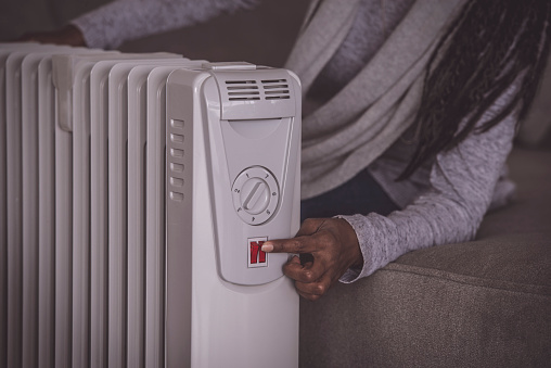 Close up image of female's hand Turning on an electric heating radiator. The woman sitting on the couch, touching on/off the red button.
