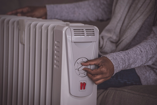 Close up image of female's hand rotating rotary switch to increase / decrease the temperature of an electric heating radiator. The woman sitting on the couch, touching on/off the rotate button.