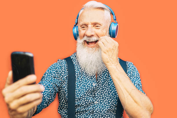 homme barbu aîné prenant le selfie avec le téléphone portable tout en écoutant la liste de lecture préférée avec le casque - mâle hipster à la mode ayant l'amusement avec des apps sociales de smartphone en plein air - vieux, concept de technologi - senior couple audio photos et images de collection