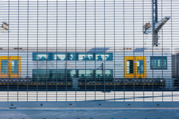 Train traveling on Sydney Harbour Bridge, view through safety fence on pedestrian walkaway, copy space, full frame horizontal composition