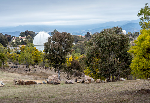 Canberra, Australia - Sep 8, 2018: Observatories and domes on a hill at the Mount Stromlo site; for the scientific study of the skies known as astronomy. Trees and grass in the foreground.