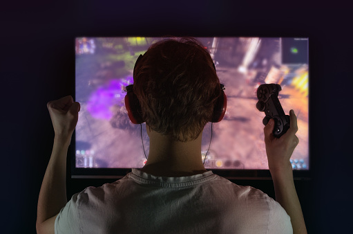 gamer with gamepad happy to win in the online game, the player with headphones in front of the monitor