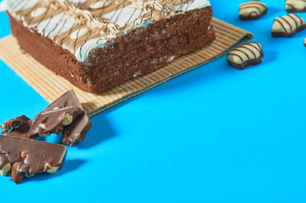 istock One whole checkered rectangular cake on bamboo mat near candy and broken chocolate bar with nuts lies on blue table on party. Celebration concept. Space for text 1200594365