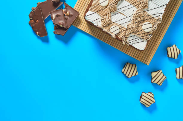 istock One whole checkered rectangular cake on bamboo mat near candy and broken chocolate bar with nuts lies on blue table on party. Celebration concept. Space for text. Top view 1200594371
