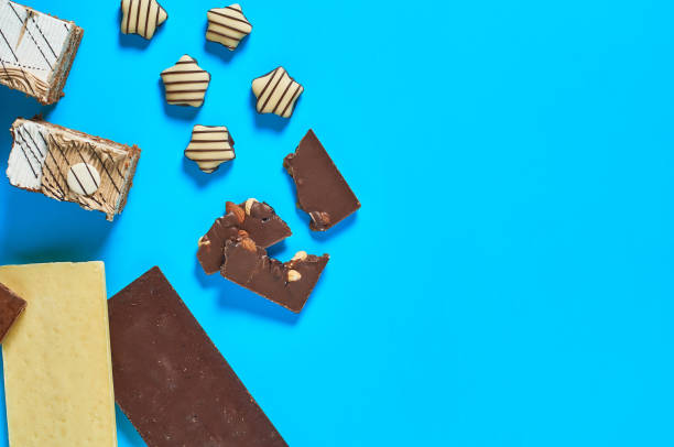 istock Sliced checkered rectangular cake near chocolate bar and candies lies on blue table on party. Celebration concept. Space for text. Top view 1200594433