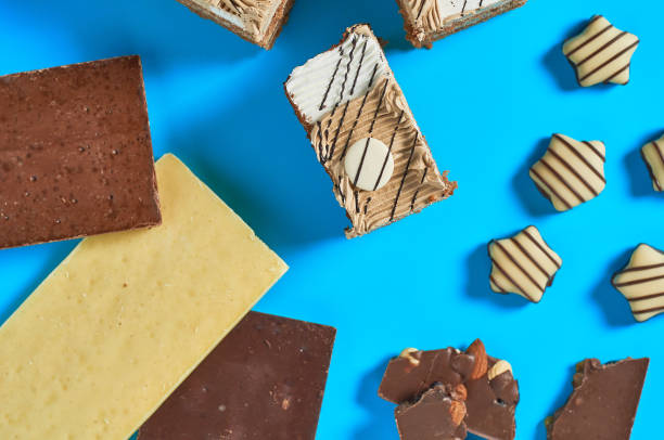 istock Sliced checkered rectangular cake near chocolate bar and candies lies on blue table on party. Celebration concept. Close-up. Top view 1200594438