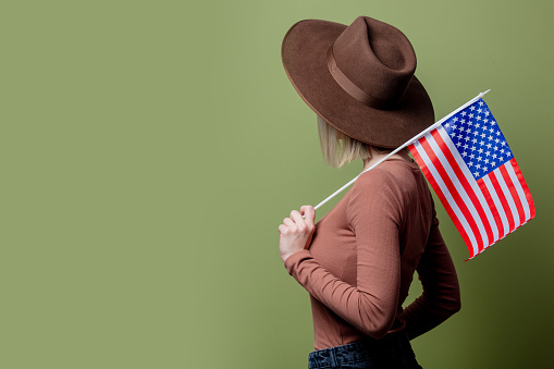 Beautiful cowgirl in a hat with United States of America flag on green background