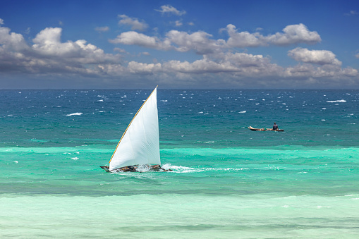 Sail boat in the sea beside the beach with blue sky and white sand.