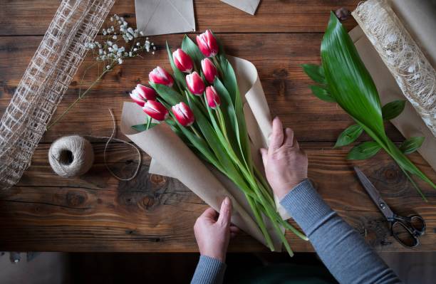 Woman Making A Bouquet Of Tulips Top view of unrecognizable woman arrange Tulips on wooden table, woman's hands creating a bouquet of flowers. florist stock pictures, royalty-free photos & images