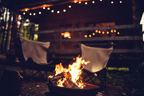 Camp fire and two empty chairs in front of a rustic chalet in Quebec