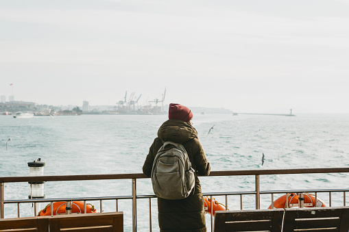 A student or tourist girl is standing on the deck or sailing on a ferry along the Bosphorus in Istanbul and enjoys beautiful views.