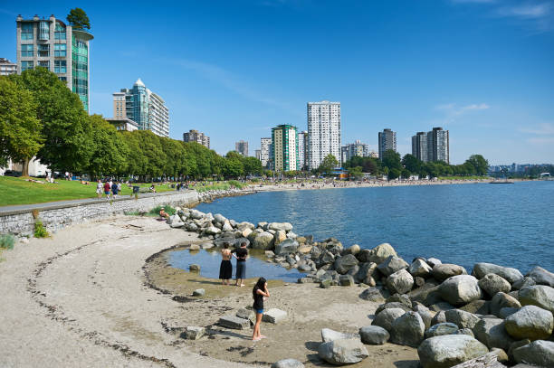 Panoramic view at English Bay with couple on beach Vancouver, British Columbia, Canada - July 18, 2012: Panoramic view at English Bay with beach and people in West End, near Morton and Stanley Park beach english bay vancouver skyline stock pictures, royalty-free photos & images