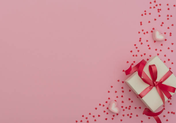 istock Valentine's Day concept. White gift box with red ribbon and two heart-shaped marshmallows on pink background with lots of small red hearts. Valentine greeting card. Flat lay style with copy space. 1200642960