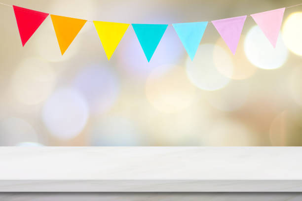 Colorful bunting party flags hanging on blur abstract bokeh light and white marble table background, birthday, greeting card background, banner, backgdrop, mock up, template, wallpaper