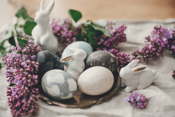 istock Happy Easter. Stylish Easter eggs on vintage plate, white bunnies and lilac flowers on rustic linen  fabric. Natural dyed easter eggs and spring flowers. Holiday decor. 1200654326