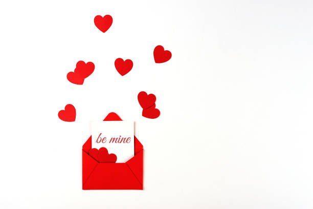 Red envelope with message note on white background, decorated with themed red confetti in the shape of heart. Valentine's day concept stock photo
